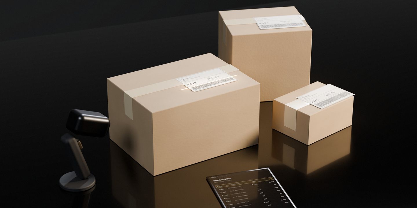 Three cardboard parcels of different sizes, labelled and ready, on a dark stone desk; a scanner’s beam on the first label and the stock position live on a tablet
