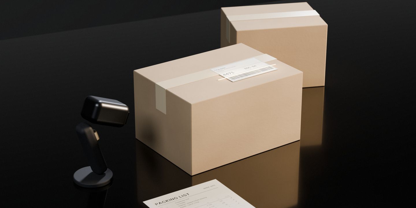 A cardboard parcel on a dark stone desk, a scanner’s beam across the barcode of its shipping label, the packing list beside it and the next parcel waiting